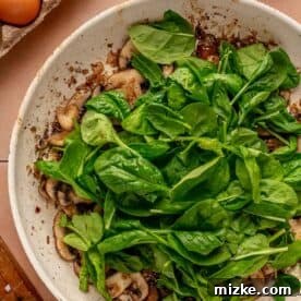 baby spinach leaves added on top of mushroom and shallot mixture in the skillet