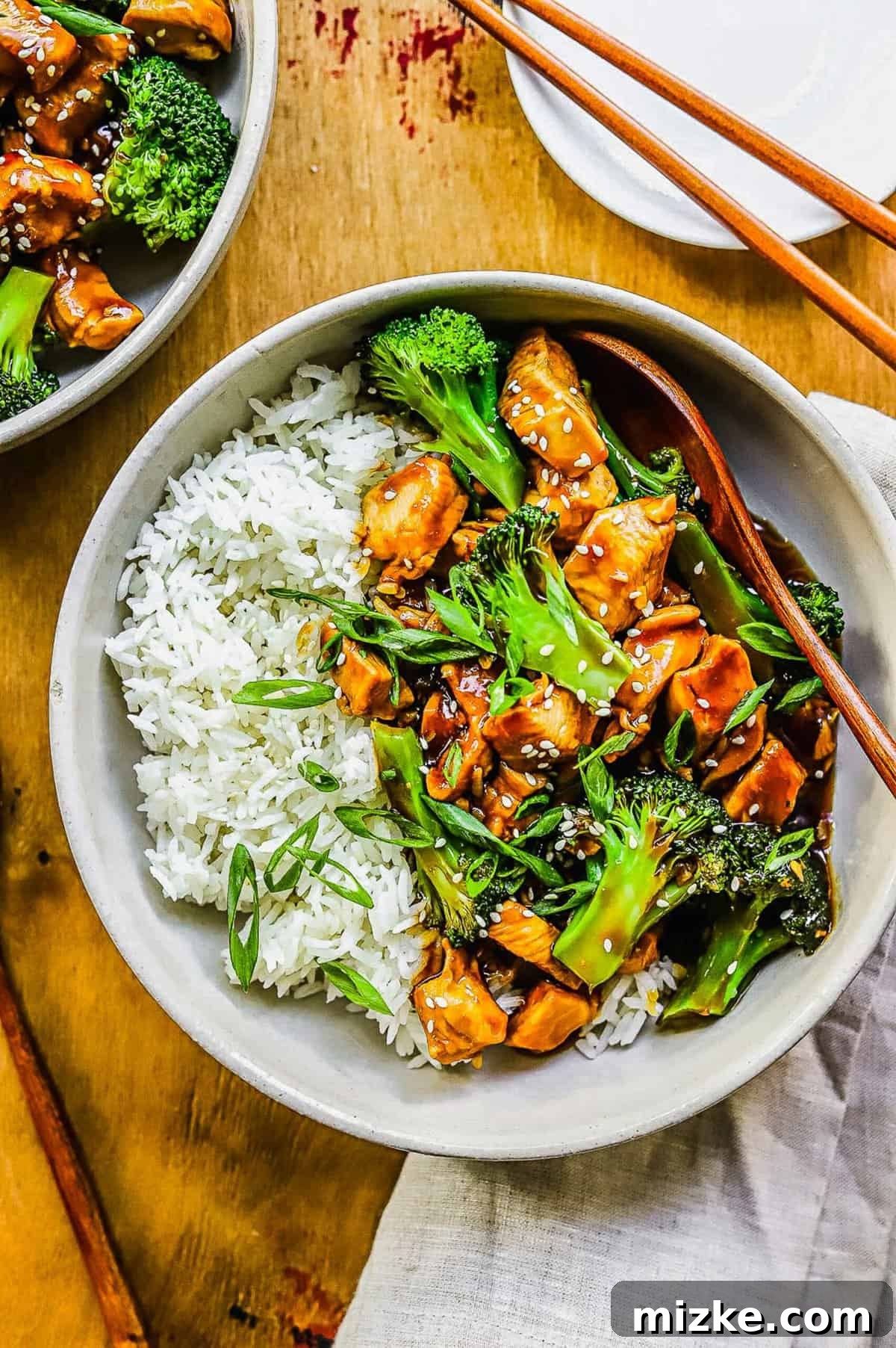 This 20-minute teriyaki chicken and broccoli recipe is made with juicy chicken and tender broccoli. It's healthy and better than takeout! overhead shot of teriyaki chicken and broccoli in a white bowl with white rice and wooden spoon