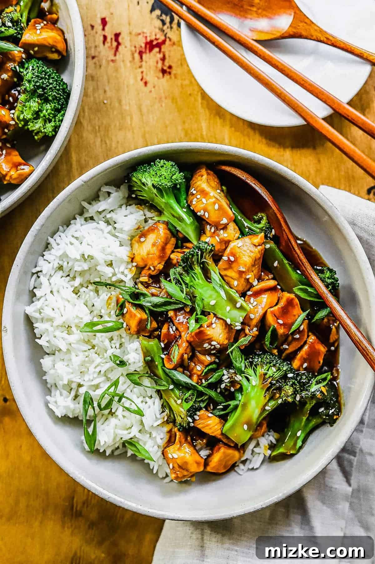 This 20-minute teriyaki chicken and broccoli recipe is made with juicy chicken and tender broccoli. It's healthy and better than takeout! overhead shot of teriyaki chicken and broccoli in a white bowl with wooden spoon