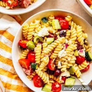 mediterranean pasta salad in a white bowl next to a gingham yellow towel