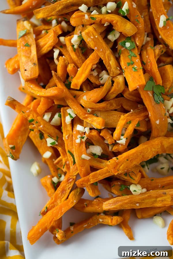 These baked garlic sweet potato fries are a great side dish for any burger or whenever the craving hits! Recipe on tablefortwoblog.com A serving of freshly baked garlic sweet potato fries, perfectly golden brown and garnished with parsley. Recipe on tablefortwoblog.com