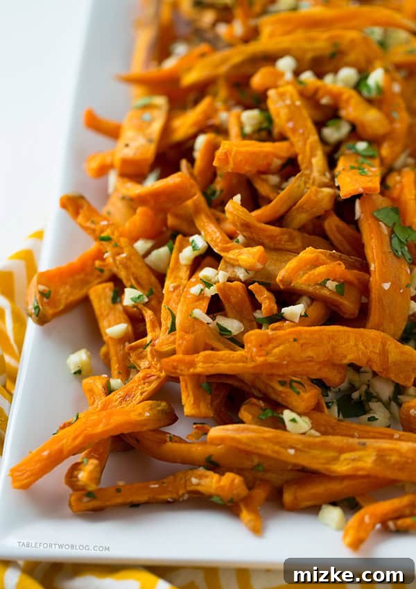These baked garlic sweet potato fries are a great side dish for any burger or whenever the craving hits! Recipe on tablefortwoblog.com Platter of baked garlic sweet potato fries with a rustic backdrop, showcasing their appetizing appeal. Recipe on tablefortwoblog.com