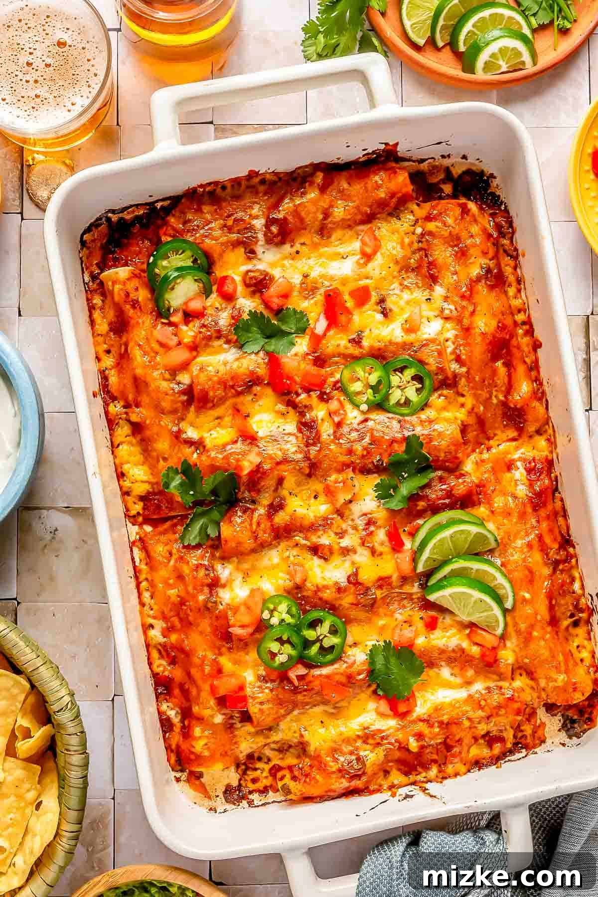 Savory Beef Enchiladas 2 Delicious beef enchiladas in a baking dish, garnished with fresh cilantro, vibrant jalapeños, and bright lime slices, with a refreshing beverage nearby.