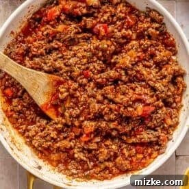 Savory Beef Enchiladas 13 ground beef mixture mixed with red enchilada sauce in a white skillet with a wooden spoon in the center