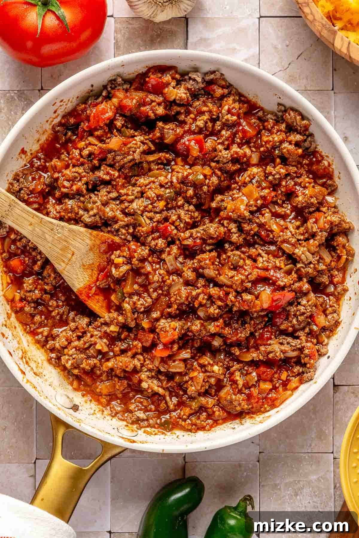Savory Beef Enchiladas 4 Ground beef mixture coated in red enchilada sauce and taco seasoning, stirred with a wooden spoon in a skillet.