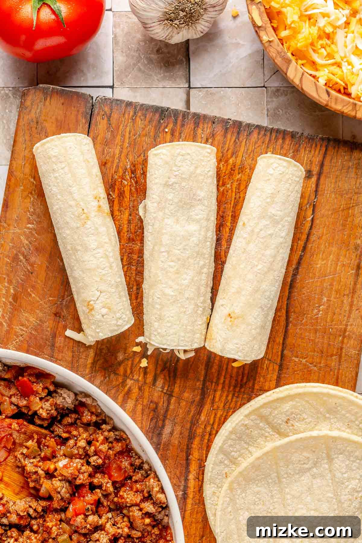 Savory Beef Enchiladas 7 Neatly rolled corn tortillas, filled with beef and cheese, placed seam-side down in a row on a cutting board, ready for the baking dish.