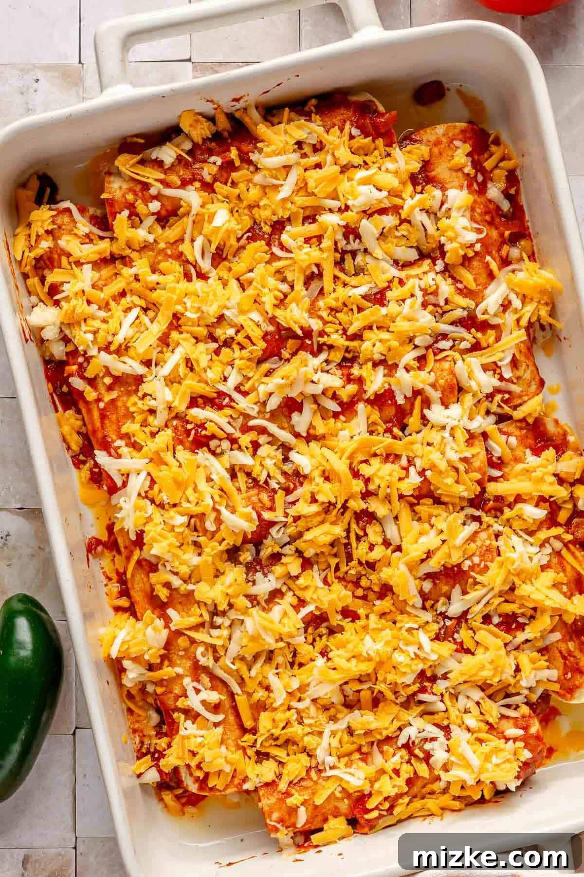 Savory Beef Enchiladas 8 A baking dish filled with assembled beef enchiladas, generously topped with rich red enchilada sauce and a sprinkle of shredded cheese, ready for the oven.