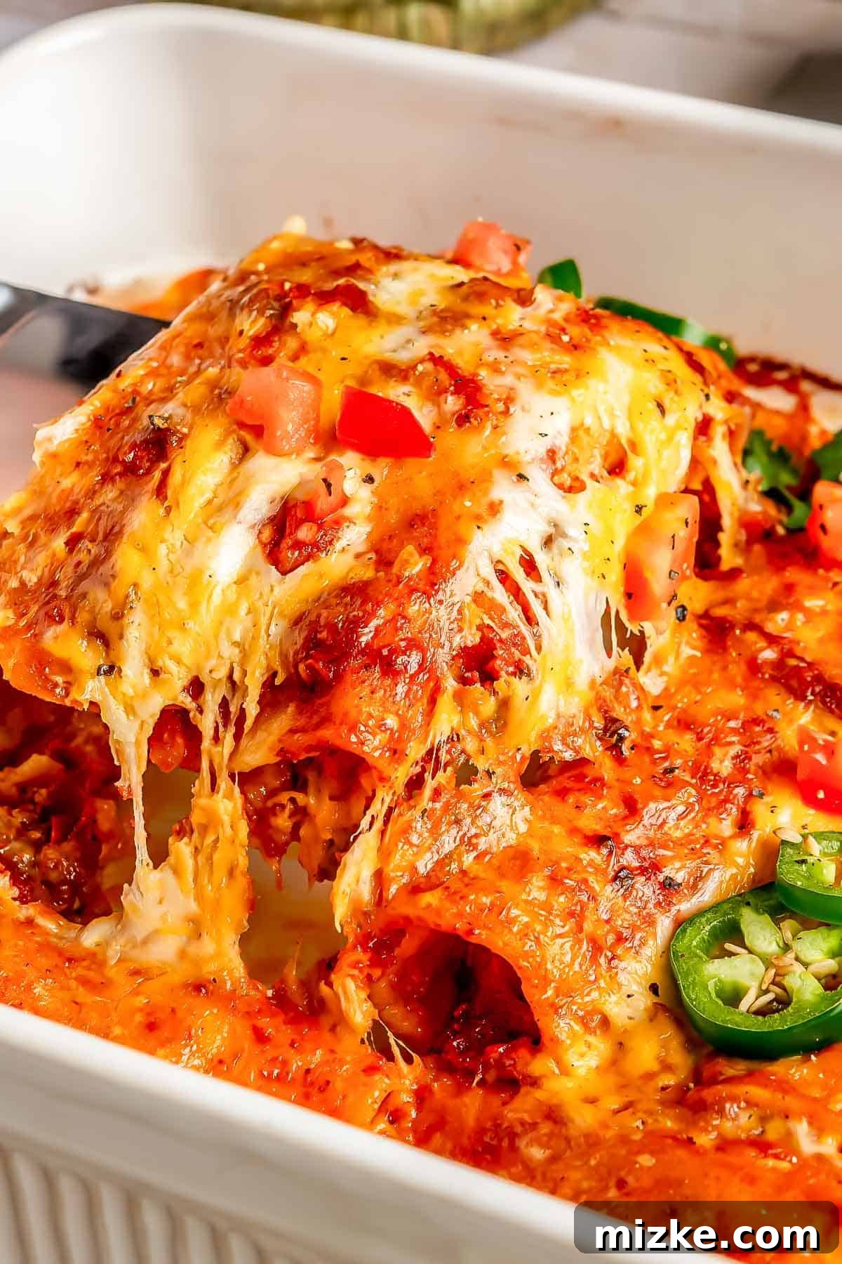 Savory Beef Enchiladas 9 Two beef enchiladas being carefully lifted from a baking dish with a serving utensil, showcasing their golden-brown top and rich filling.