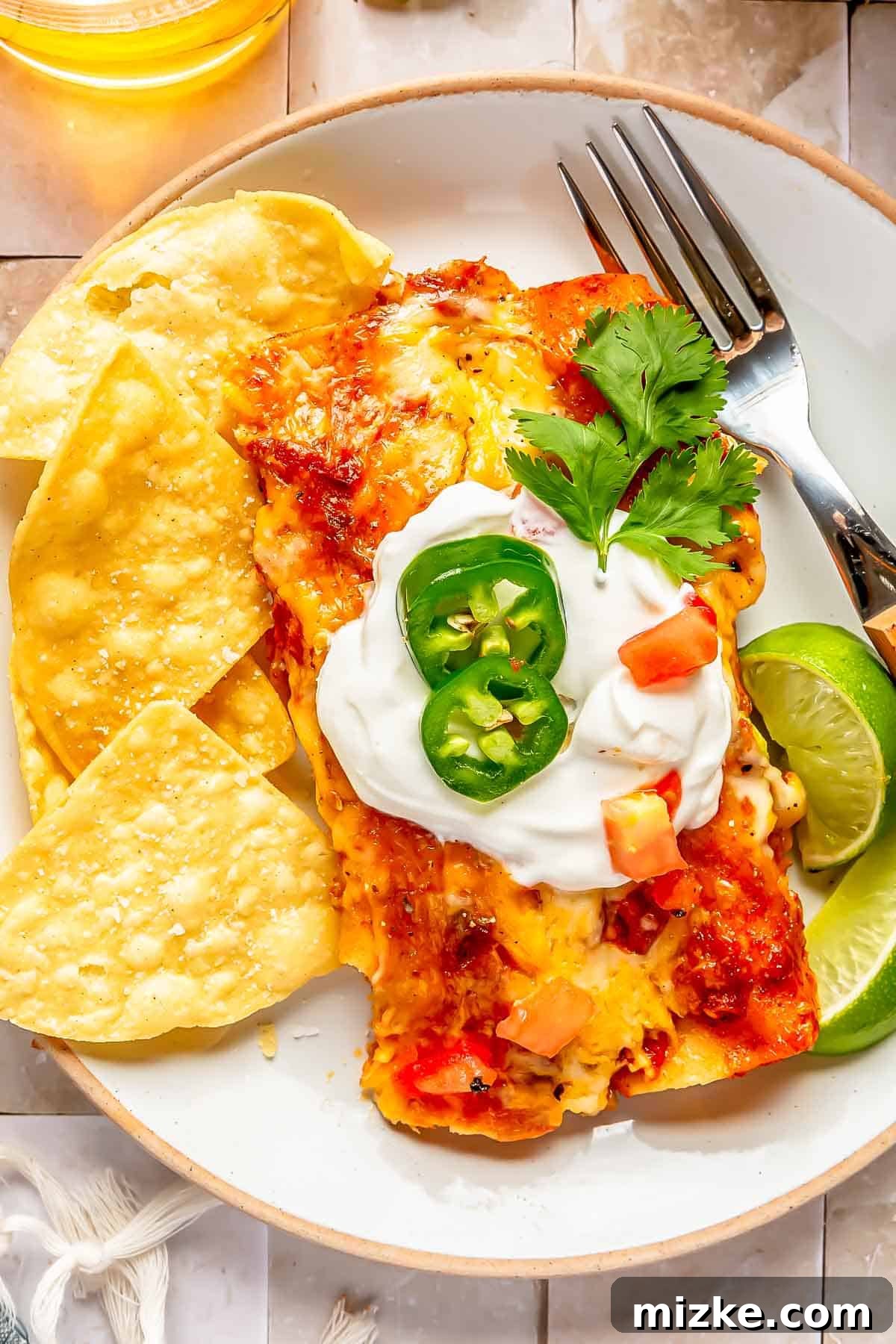 Savory Beef Enchiladas 10 Two perfectly plated beef enchiladas on a white dish, elegantly topped with cool sour cream, fiery jalapeños, and fresh diced tomatoes, served alongside crispy corn tortilla chips and bright lime wedges.
