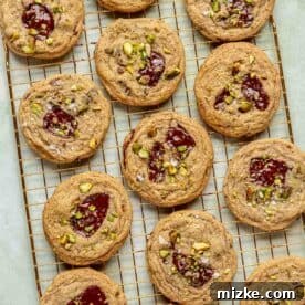 Freshly baked chocolate chip pistachio cookies are arranged neatly on a gold wire cooling rack, allowing them to cool down evenly.
