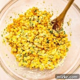 a wooden spoon in a clear bowl stirs together the corn fritter batter
