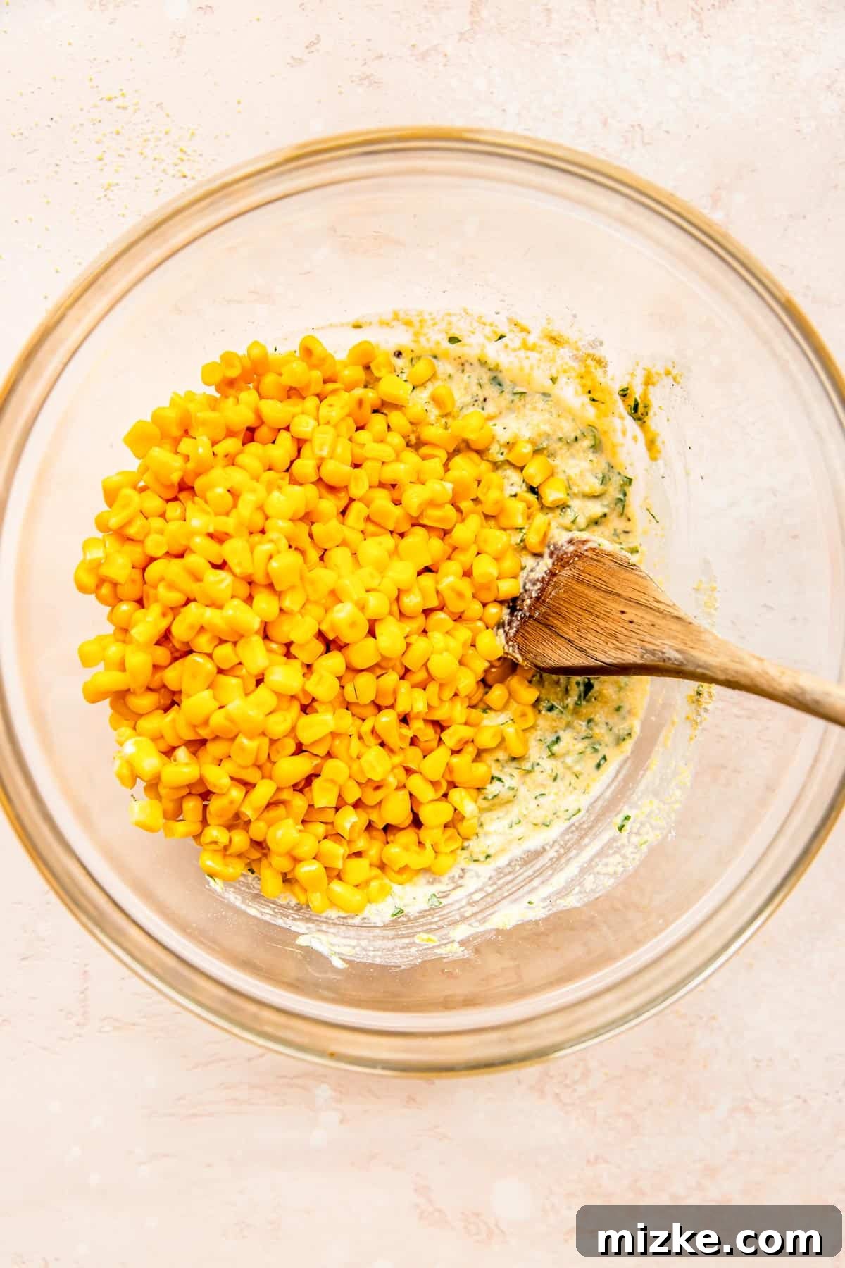 Smoky Sweet Corn Bites 5 Sweet corn kernels are carefully added to the freshly prepared corn fritter batter in a clear mixing bowl.