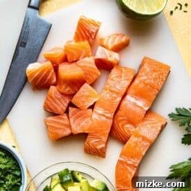 Fresh salmon fillets being diced into cubes on a cutting board, surrounded by limes and avocados, ready for ceviche preparation.