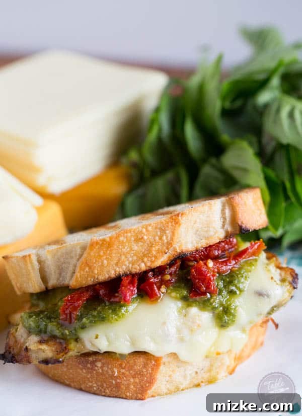 A close-up shot of a golden-brown grilled pesto chicken sandwich, filled with melted Land O Lakes Sharp Cheddar and vibrant sundried tomatoes.