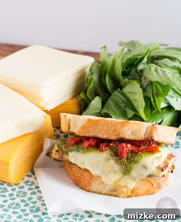 The process of layering the grilled pesto chicken, melted cheddar, and sundried tomatoes between two slices of golden bread.