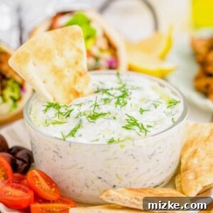 Creamy Homemade Tzatziki 7 Tzatziki dip in glass bowl on plate with pita chips, olives, and halved grape tomatoes