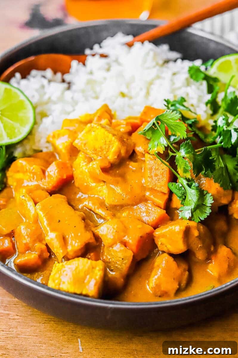 Comforting Slow Cooker Chicken Pumpkin Curry 3 A close-up shot of a serving of pumpkin coconut curry, garnished with fresh lime wedges and vibrant cilantro leaves in a black bowl.