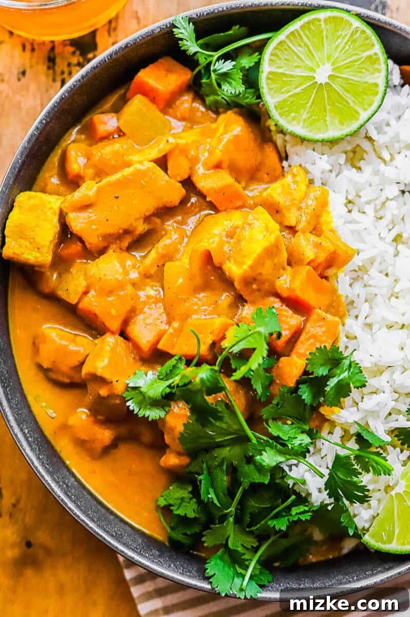 Comforting Slow Cooker Chicken Pumpkin Curry 4 A close-up view of a bowl of fluffy white rice topped with a vibrant chicken pumpkin curry, beautifully garnished with fresh cilantro leaves.