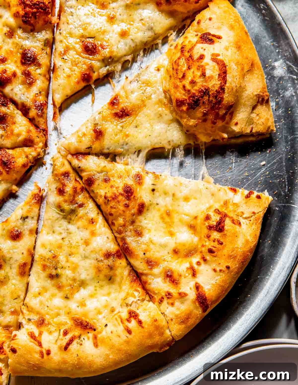 Bianco Bliss 3 A golden-crusted white pizza on a round metal tray, partially sliced with one melted cheese-filled slice pulled away, ready to be served.
