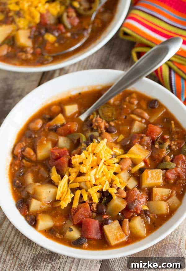 Hearty Chorizo Potato and Double Bean Crockpot Chili 4 A bowl of slow cooker chorizo, potato, and two-bean chili, topped with freshly grated cheese, ready to be served.