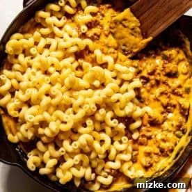 Smoky Chorizo Mac and Cheese 11 A skillet with cooked cavatappi pasta partially mixed into a creamy, cheesy ground beef sauce, with a wooden spatula resting inside.