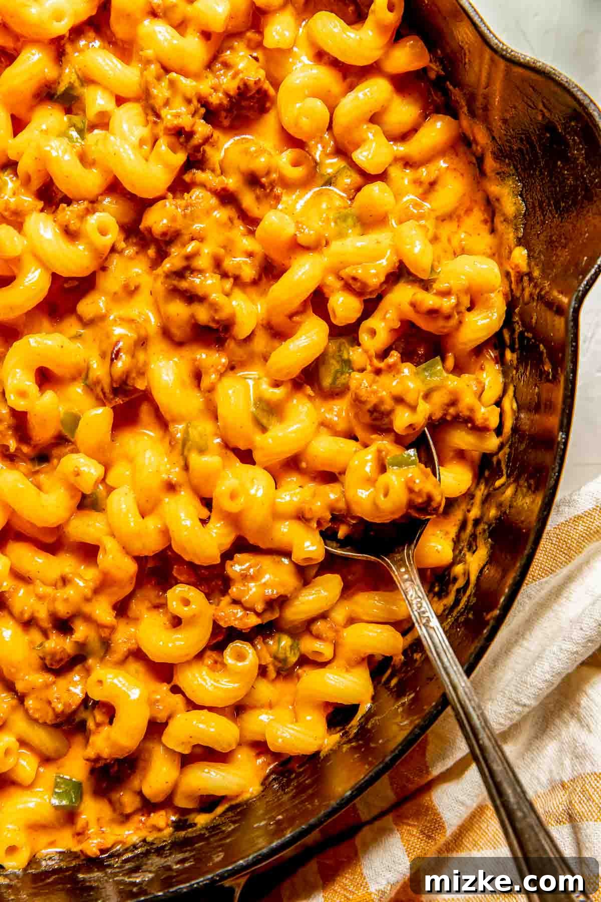 Smoky Chorizo Mac and Cheese 3 A close-up shot of a skillet filled with cheesy macaroni pasta generously mixed with savory ground chorizo, with a metal spoon resting inside.