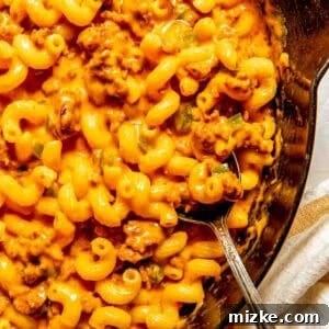 Smoky Chorizo Mac and Cheese 5 A skillet filled with cheesy macaroni pasta mixed with ground chorizo and a metal spoon resting inside.