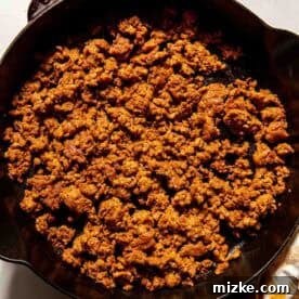 Smoky Chorizo Mac and Cheese 6 Cooked and seasoned ground meat in a black Staub skillet on a white surface, with a yellow and white striped cloth nearby.