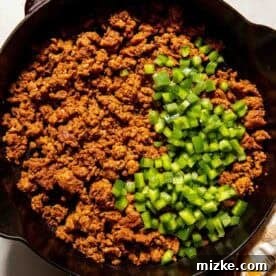 Smoky Chorizo Mac and Cheese 7 Cooked ground meat and diced green bell peppers in a black Staub skillet, viewed from above.