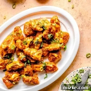 Bang bang chicken on a serving platter bext to a bowl of bang bang sauce, a bowl of pepper, and a knife chopping scallions.