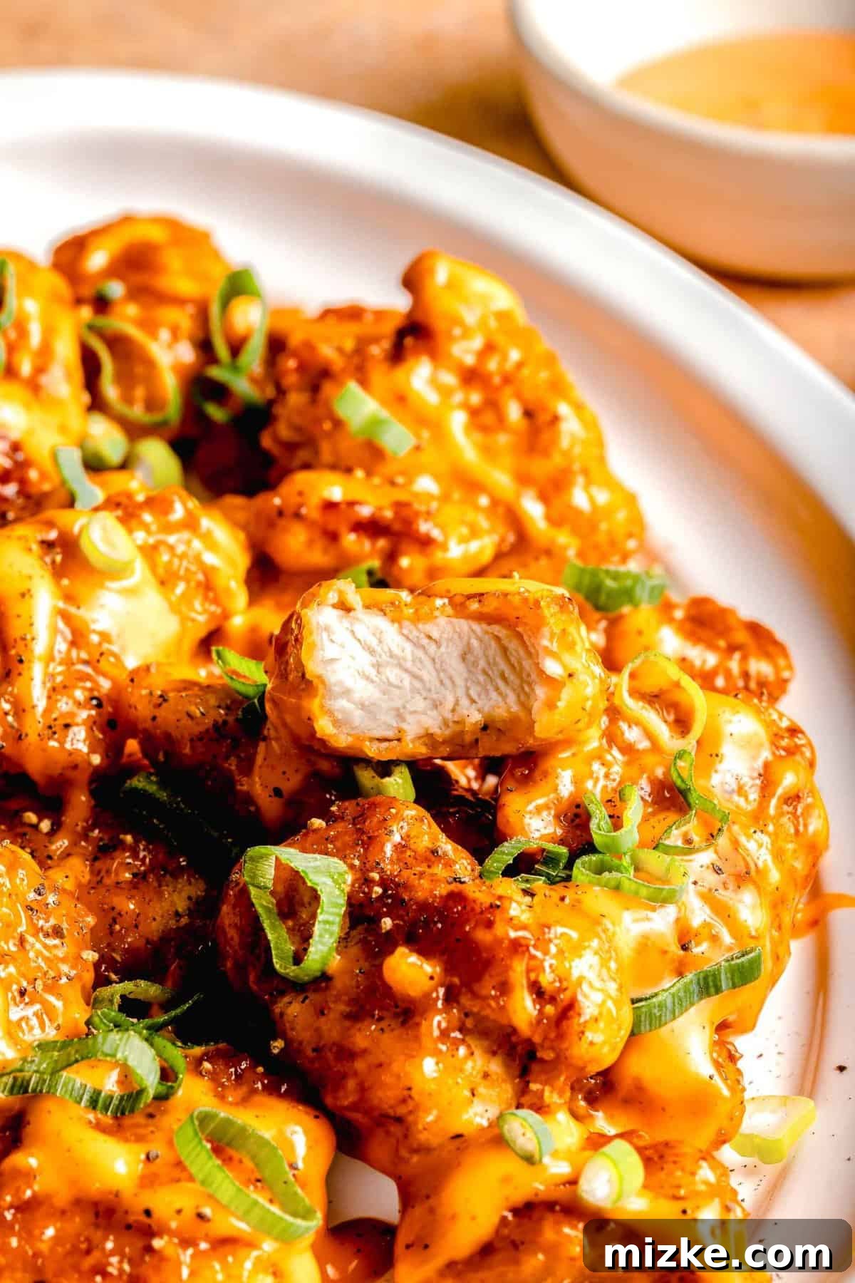 This bang bang chicken dish really lives up to its name. It is A close-up shot of Bang Bang Chicken on a white plate, with one piece clearly showing a bite taken out, revealing the succulent chicken inside its crispy, sauce-coated breading.