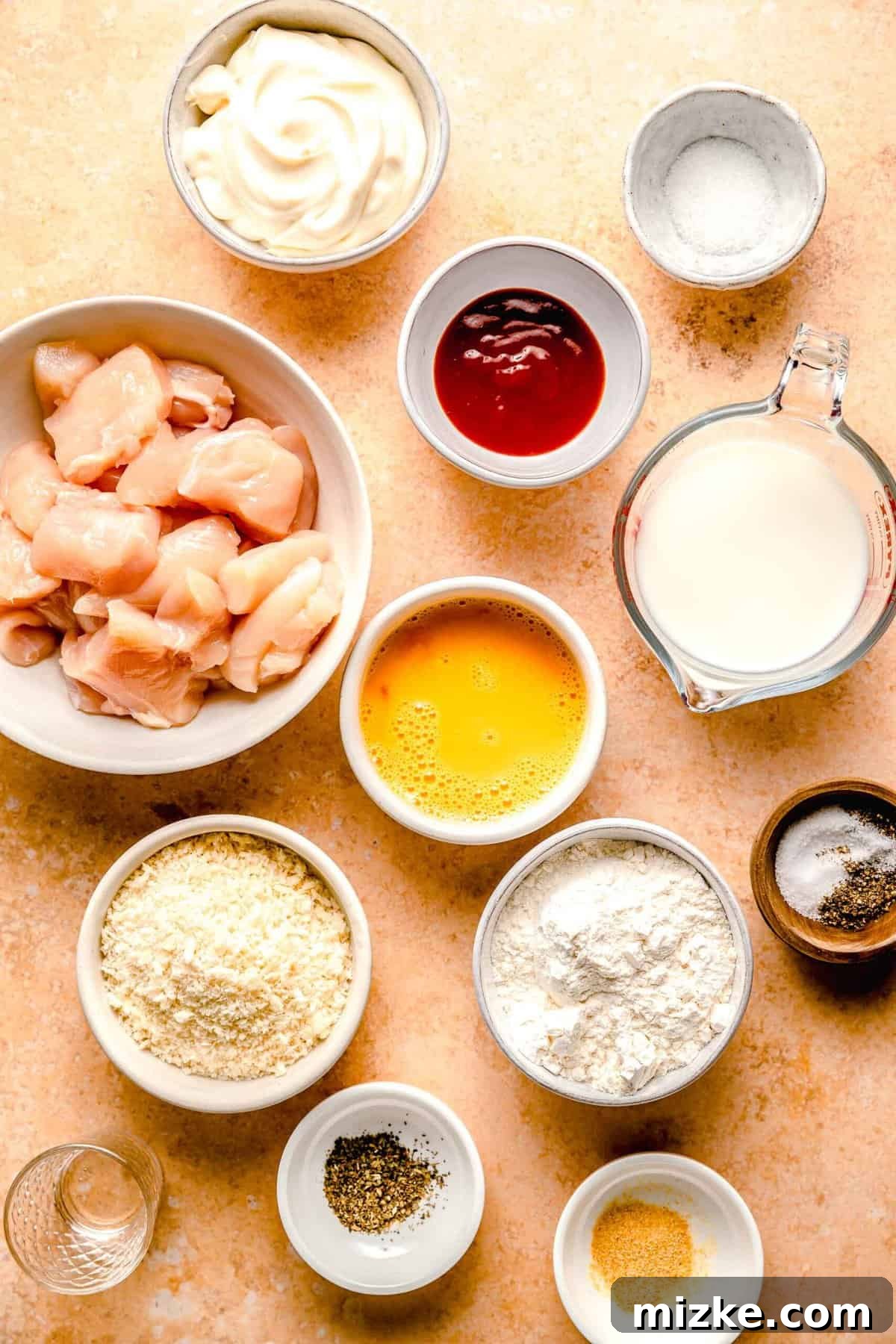 This bang bang chicken dish really lives up to its name. It is Various ingredients for Bang Bang Chicken, including cubed chicken, Sriracha, mayonnaise, and spices, neatly arranged in separate bowls on a kitchen counter, ready for preparation.
