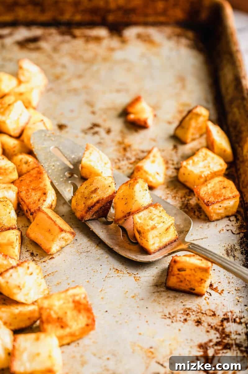 Roasted Potato Perfection 4 roasted cubed potatoes on a serving spoon on a metal baking sheet, showing their delicious texture