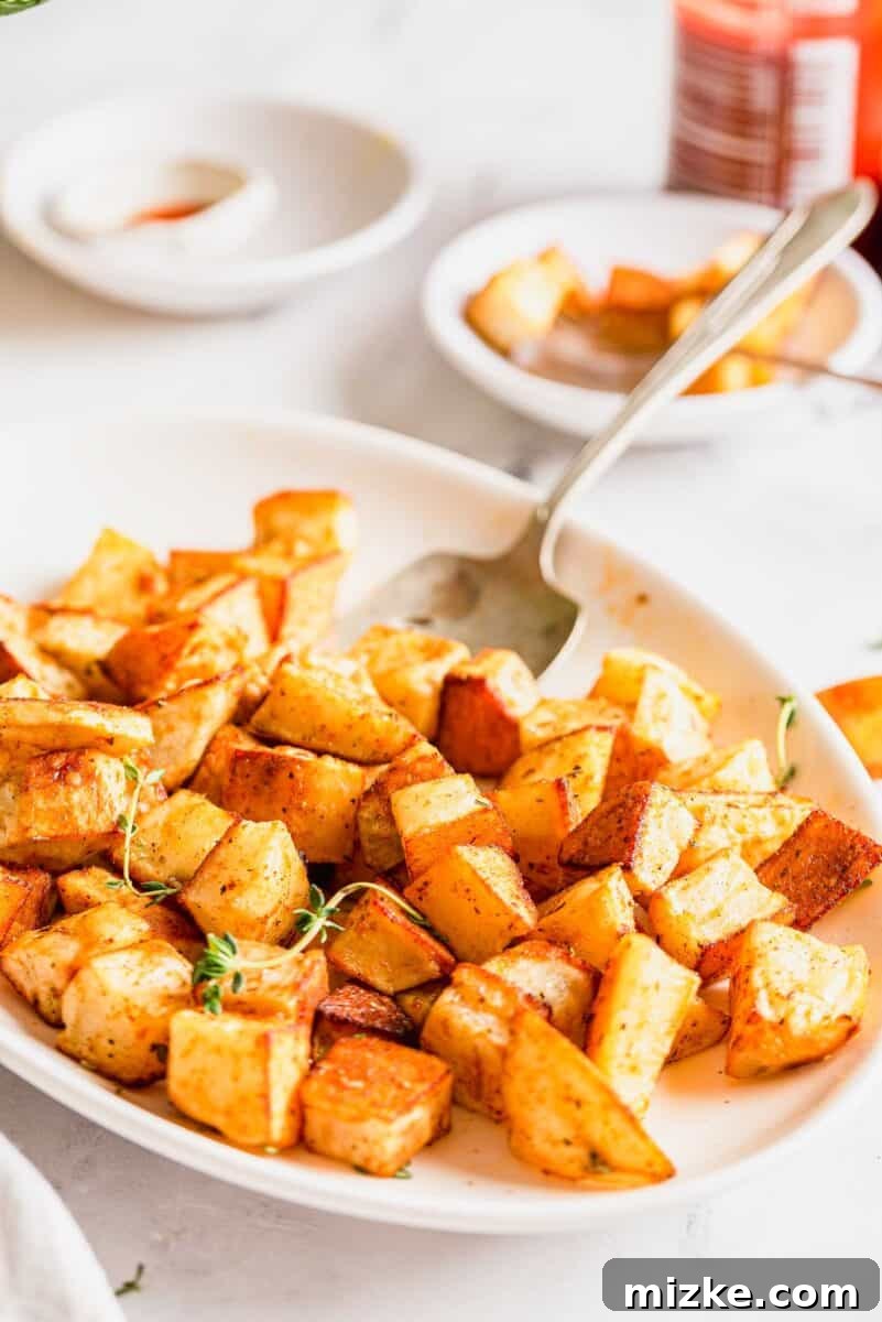 Roasted Potato Perfection 6 roasted potatoes on a large white platter with a serving spoon on the platter. the roasted potatoes are garnished with fresh thyme, ready for serving.