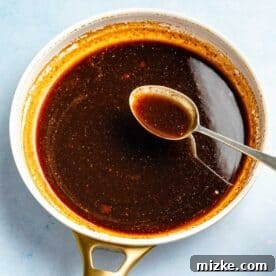 Chipotle Honey Glazed Chicken Bites 4 The rich and flavorful chipotle honey sauce simmering gently in a small saucepan, being stirred with a metal spoon.