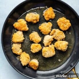 Chipotle Honey Glazed Chicken Bites 6 Golden brown breaded chicken thigh pieces sizzling in hot vegetable oil during shallow frying in a skillet.