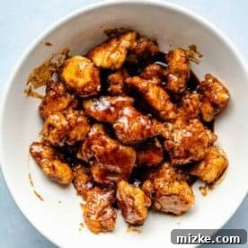 Chipotle Honey Glazed Chicken Bites 7 Crispy fried chicken poppers being thoroughly tossed in a glistening chipotle honey sauce within a large white bowl, ensuring complete coating.