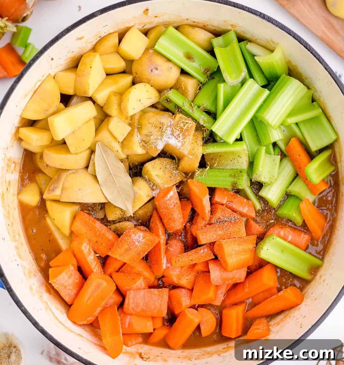 Hearty Slow Cooker Guinness Beef Stew 7 A mix of fresh potatoes, celery, carrots, thyme, salt, and bay leaves neatly arranged in a cast iron skillet, showcasing the vibrant vegetable base for the stew.