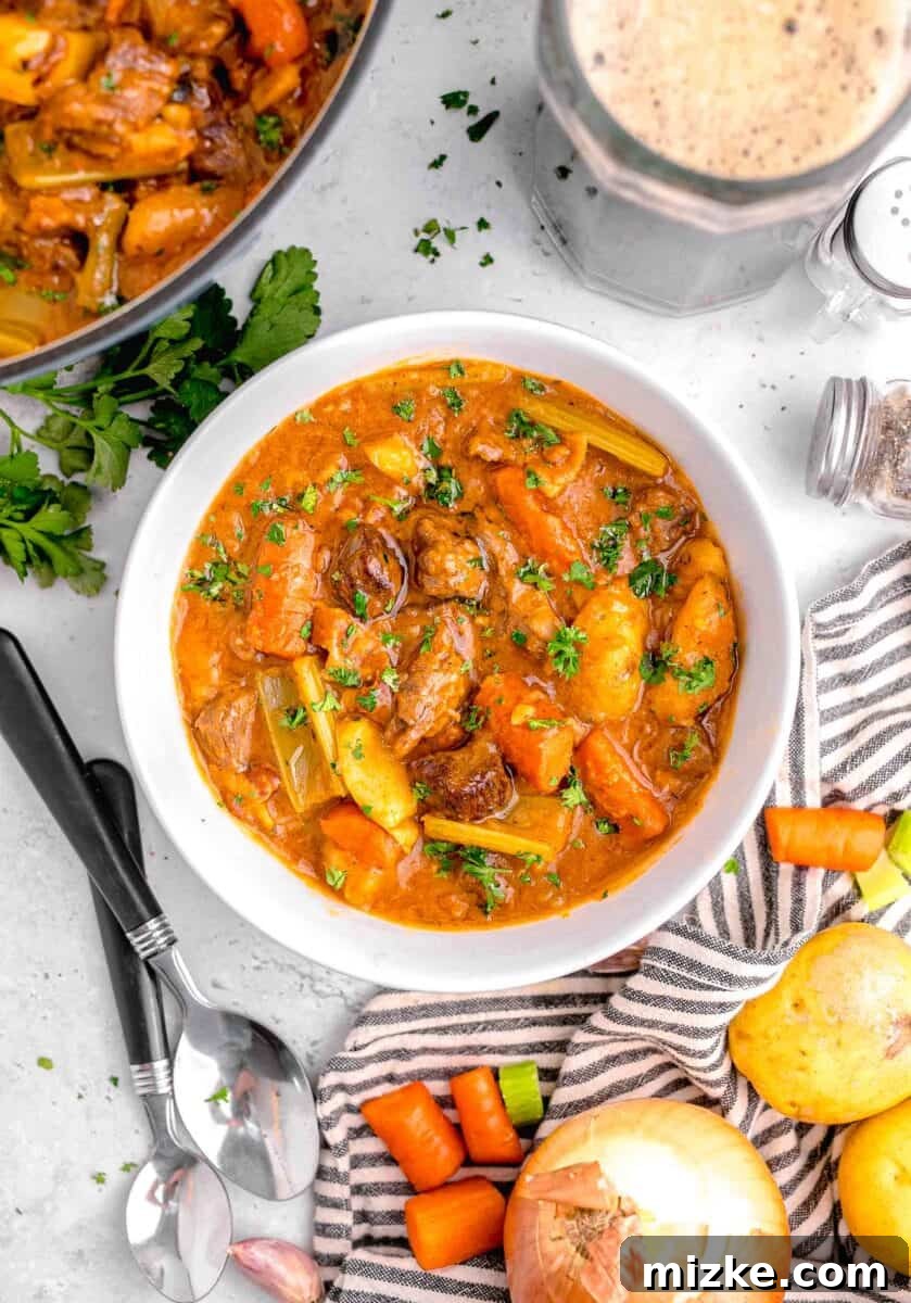 Hearty Slow Cooker Guinness Beef Stew 9 An inviting overhead view of a steaming bowl of beef stew, surrounded by fresh herbs, bread, and cutlery, perfectly set for a comforting meal.