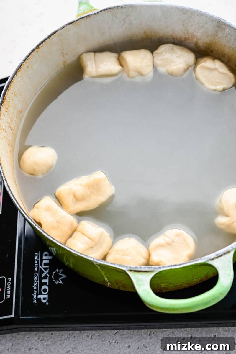 Small, unbaked pretzel bites being carefully dropped into a pot of boiling water infused with baking soda.