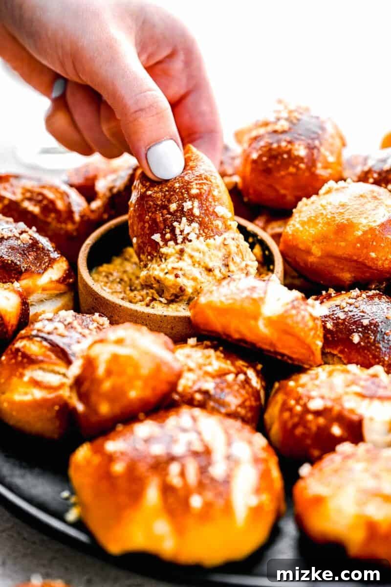 A single warm pretzel bite being dipped into a dollop of coarse whole-grain mustard.