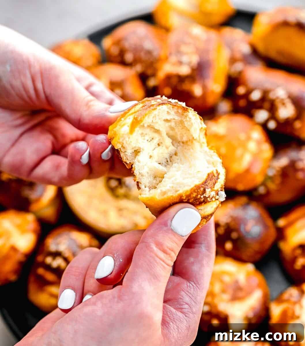 A hand gently tearing a freshly baked pretzel bite in half, revealing its soft, airy interior texture.
