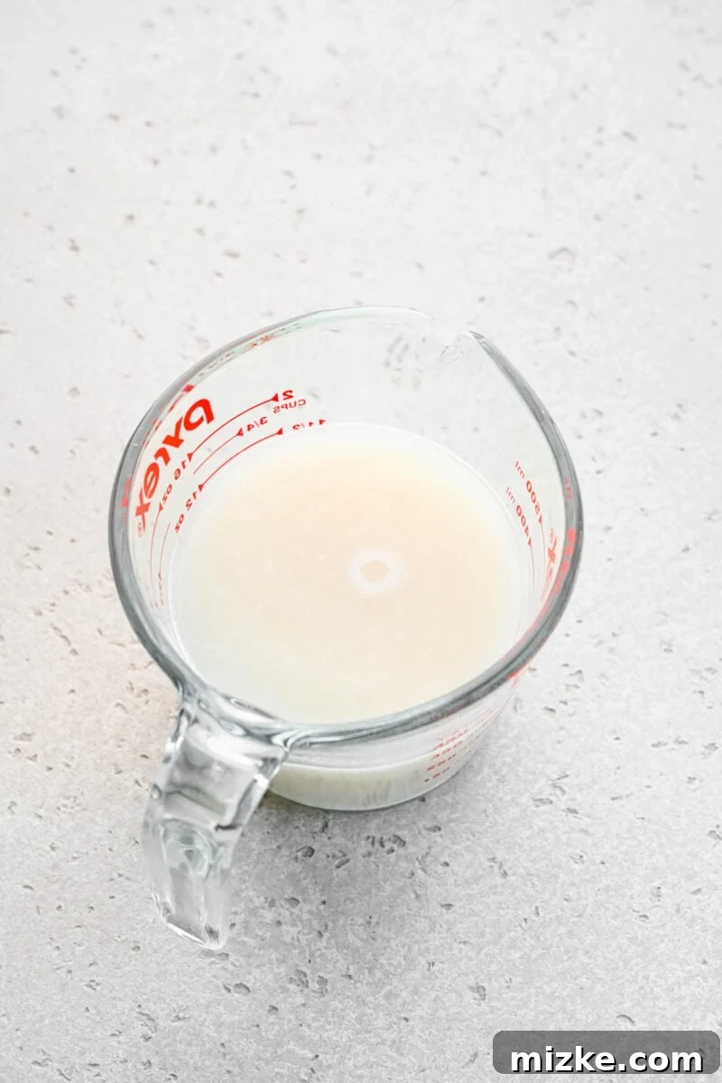 Close-up shot of active dry yeast dissolving in warm water within a clear glass measuring cup, showing the initial activation process.
