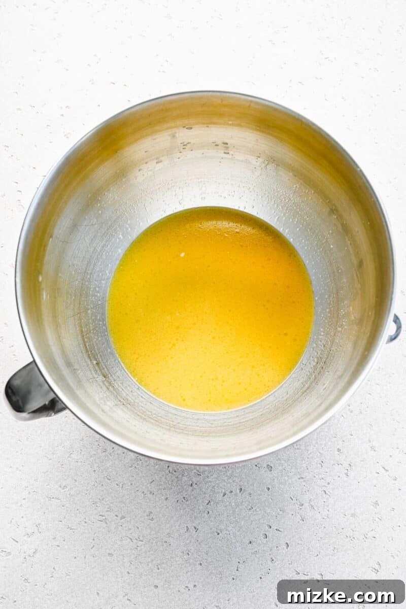 Wet ingredients for pretzel dough, including activated yeast, melted butter, and brown sugar, combined in a stand mixer bowl.