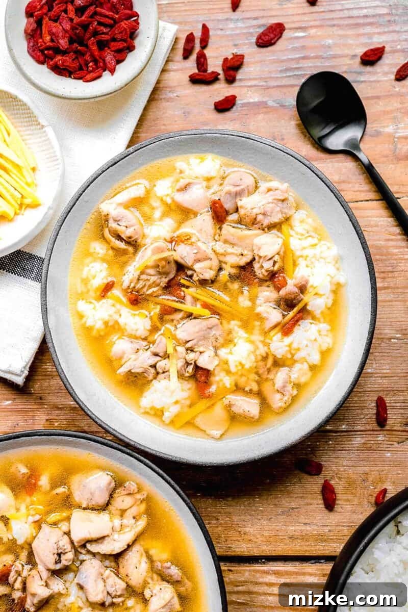 Soul-Warming Rice Wine Chicken Soup 2 Drunken Chinese chicken soup with white rice in a white ceramic bowl next to smaller bowls of ingredients and a metal black spoon, embodying warmth and comfort