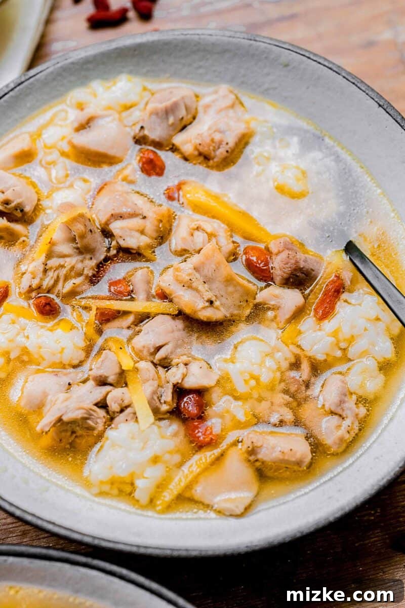 Soul-Warming Rice Wine Chicken Soup 5 Drunken Chinese chicken soup in a white bowl with a spoon resting in it, inviting you to enjoy its warmth and flavor.