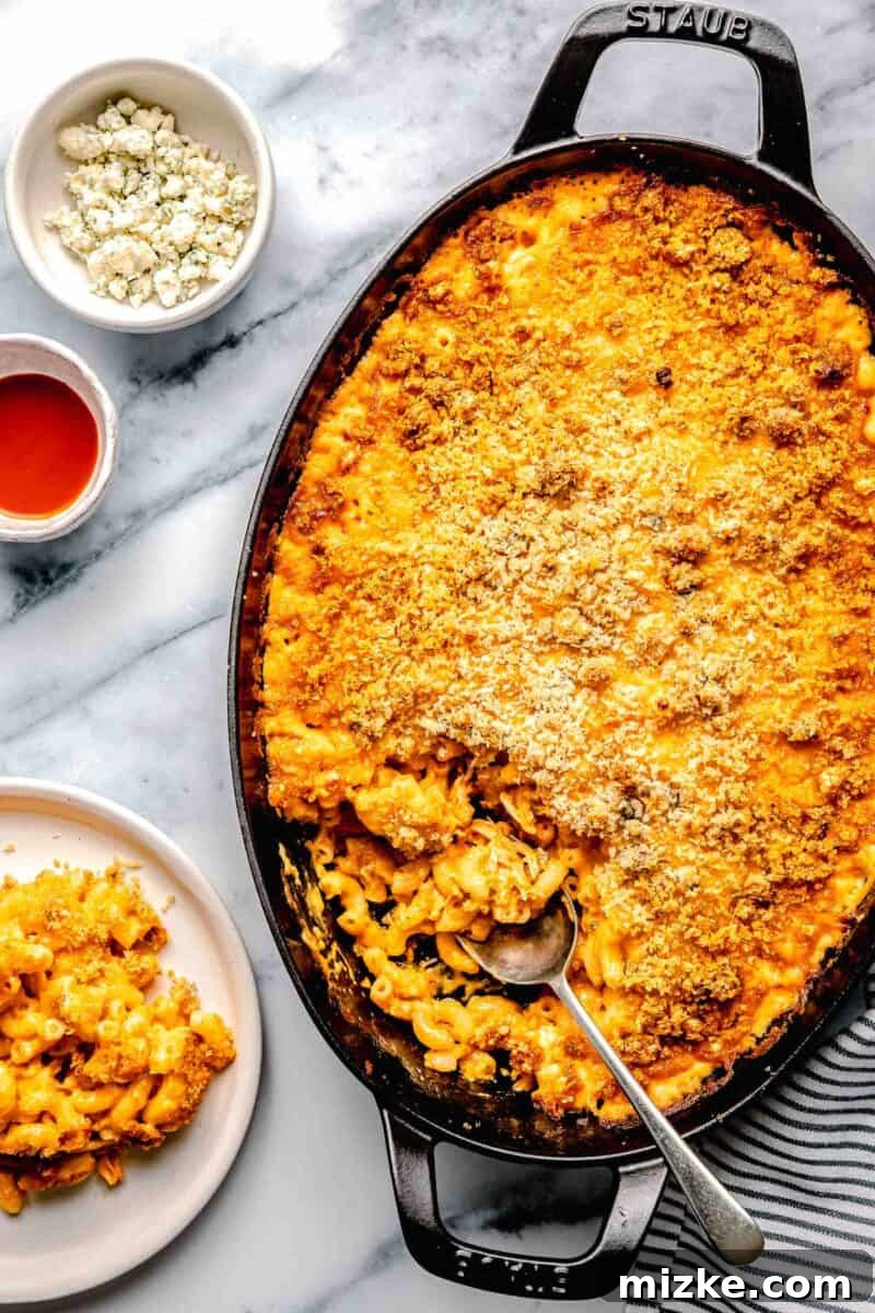 Kickin' Buffalo Mac and Cheese 2 A spoon is placed inside a generous dish filled with golden-brown Buffalo Chicken Mac and Cheese, showcasing its creamy texture and rich topping.