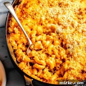 A spoon is placed in a large dish filled with mac and cheese.