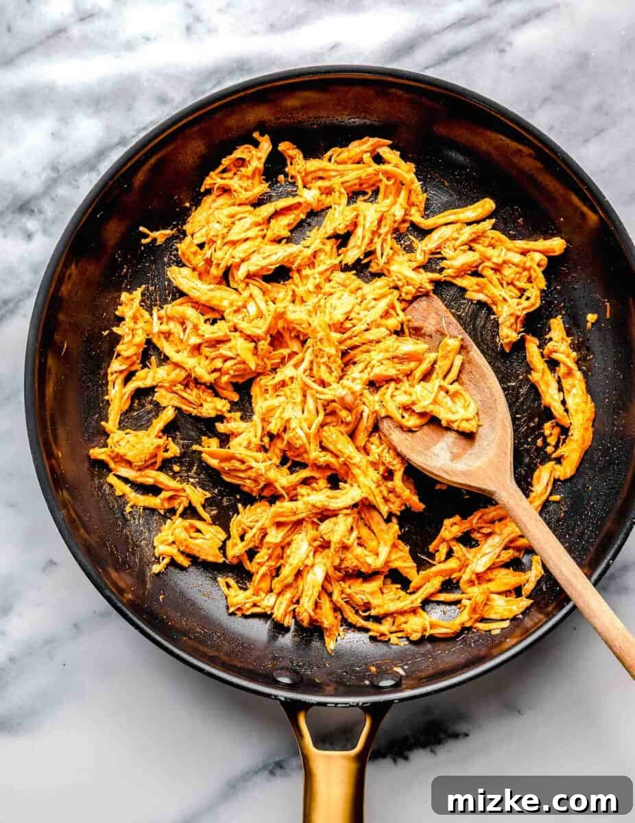 Kickin' Buffalo Mac and Cheese 4 Shredded chicken pieces are being sautéed with minced garlic in a large skillet over medium-high heat.