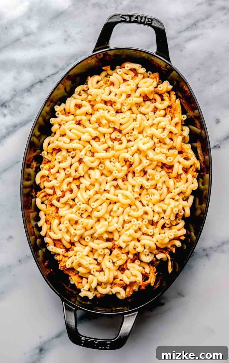 Kickin' Buffalo Mac and Cheese 6 Al dente macaroni noodles are evenly spread at the bottom of a large glass baking dish, ready for layering.